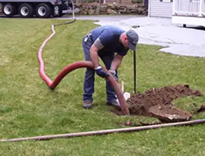 Septic pumping technician servicing a residential septic tank with a vacuum hose in Portland, OR