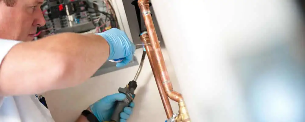 Water heater repair technician testing copper pipe connections and controls in Portland, OR